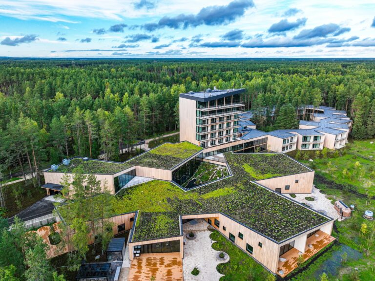 Kurro Spa from above: the star-shaped building with a green roof, the tower and the ring-shaped wing, forest to the horizon all around, drone view