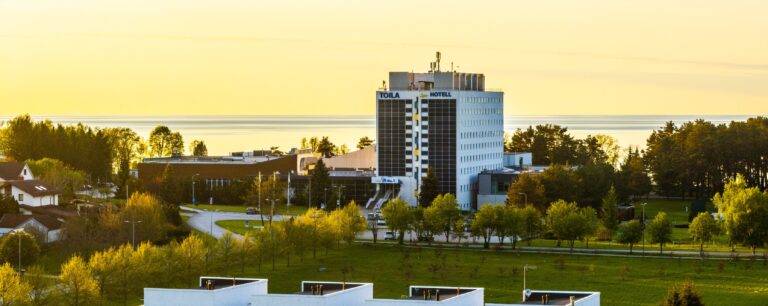 Отель Toila Spa на фоне золотого закатного неба и моря, на переднем плане деревья парка, панорама с дрона