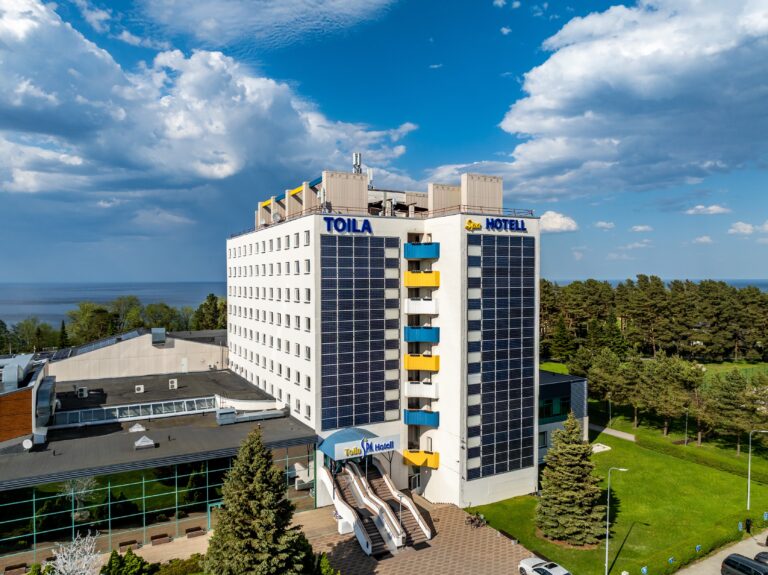 Главное здание отеля Toila Spa вблизи сверху: вывески под крышей, балконы и лестница к главному входу, позади море