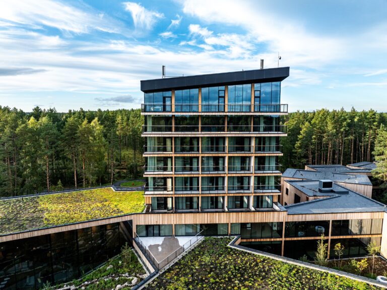 The Kurro Spa tower up close: a glass facade with balconies and a dark roof edge, green roofs below and pine forest behind