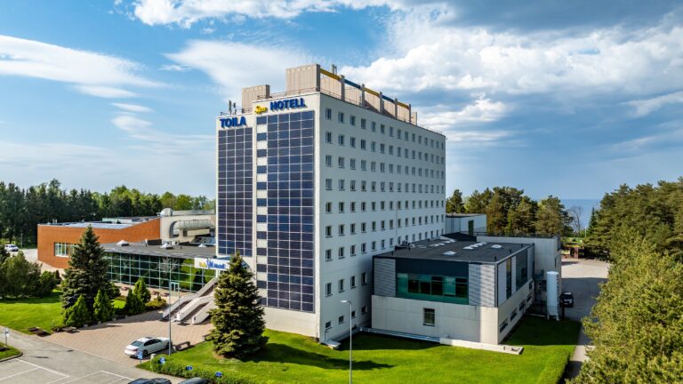 Главное здание отеля Toila Spa сбоку вместе с низким крылом, вокруг ели и газон, облачное весеннее небо, вид с дрона