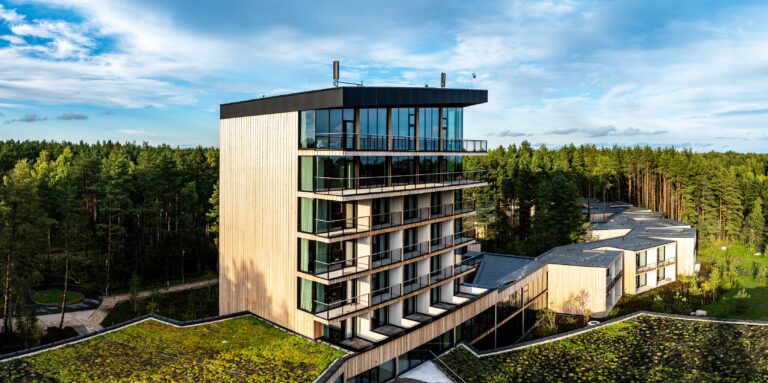 The Kurro Spa tower from the side: a timber-clad end wall and balconies, the lower curving wing beside it, drone panorama