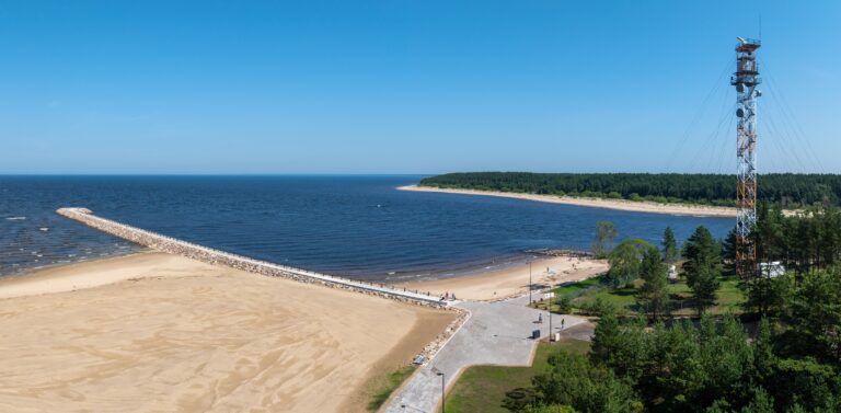 The Narva-Jõesuu breakwater from the beach side: the sandy beach, the start of the breakwater and a mast, the far bank of the river mouth behind, drone panorama