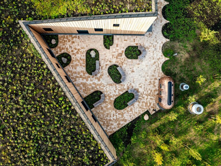 The triangular paved courtyard of Kurro Spa with rounded planting islands from directly above, green roof around it, drone view