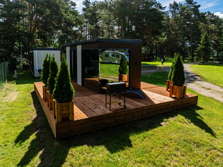 Peegelmaja otsasein peegeldab muru ja puid, terrassil grill ja elupuud, taga männid