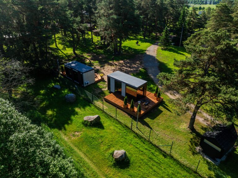 Kaks peegelmaja terrassidega metsa ja muru piiril, kõrval rändrahnud, droonivaade ülalt