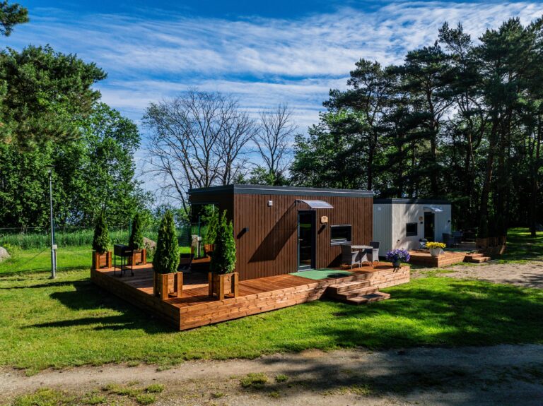 Kaks Toila Spa peegelmaja kõrvuti, tumeda ja heleda voodriga, ees kruusatee ja muru, droonivaade