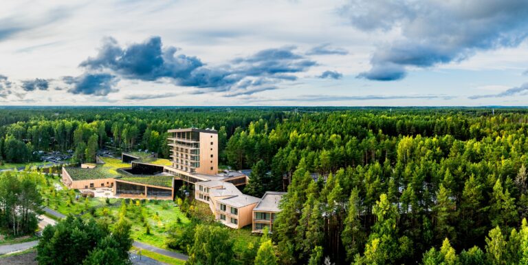 The Kurro Spa complex in the middle of the forest under a cloudy sky, wide drone panorama