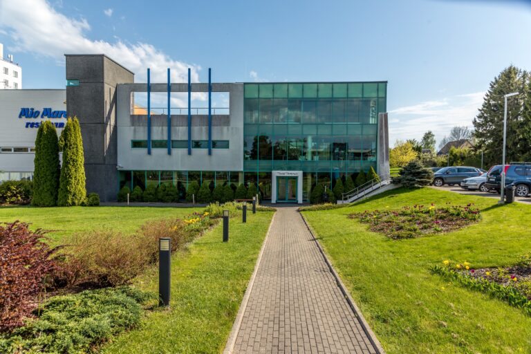 Мощёная пешеходная дорожка через озеленение ко входу в здание Toila Spa с зелёным стеклянным фасадом