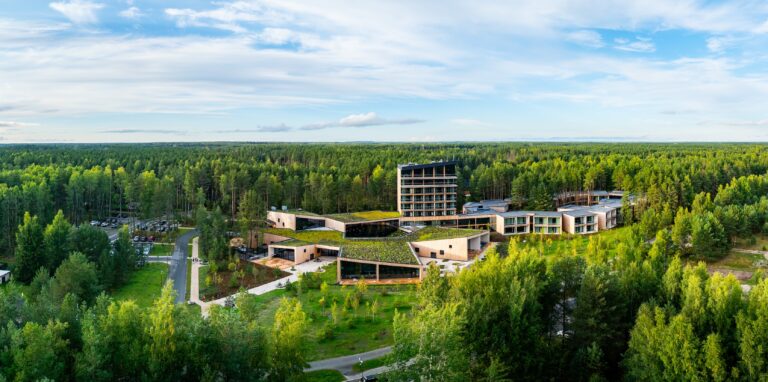 Kurro Spa with its green roofs and tower, pine forest all the way to the horizon, drone panorama