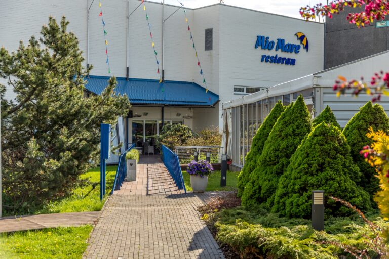 Вход в ресторан Mio Mare в здании Toila Spa: синий навес, пандус и туи
