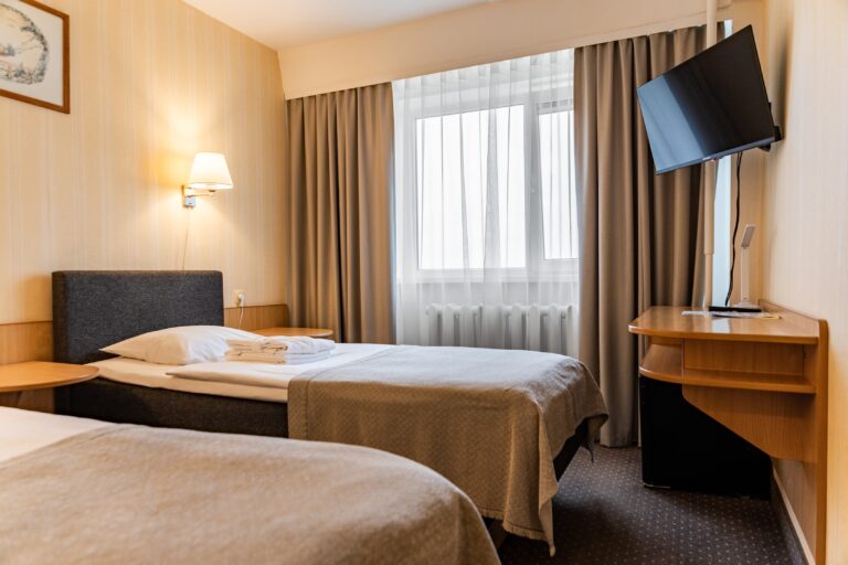 A Toila Spa hotel room with two beds, a desk and a television, light curtains at the window