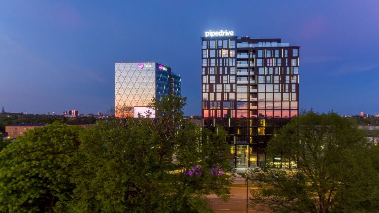 Woho kaks büroohoonet kerkivad sinisel tunnil puulatvade kohale, fassaadidel Pipedrive'i ja Telia sildid